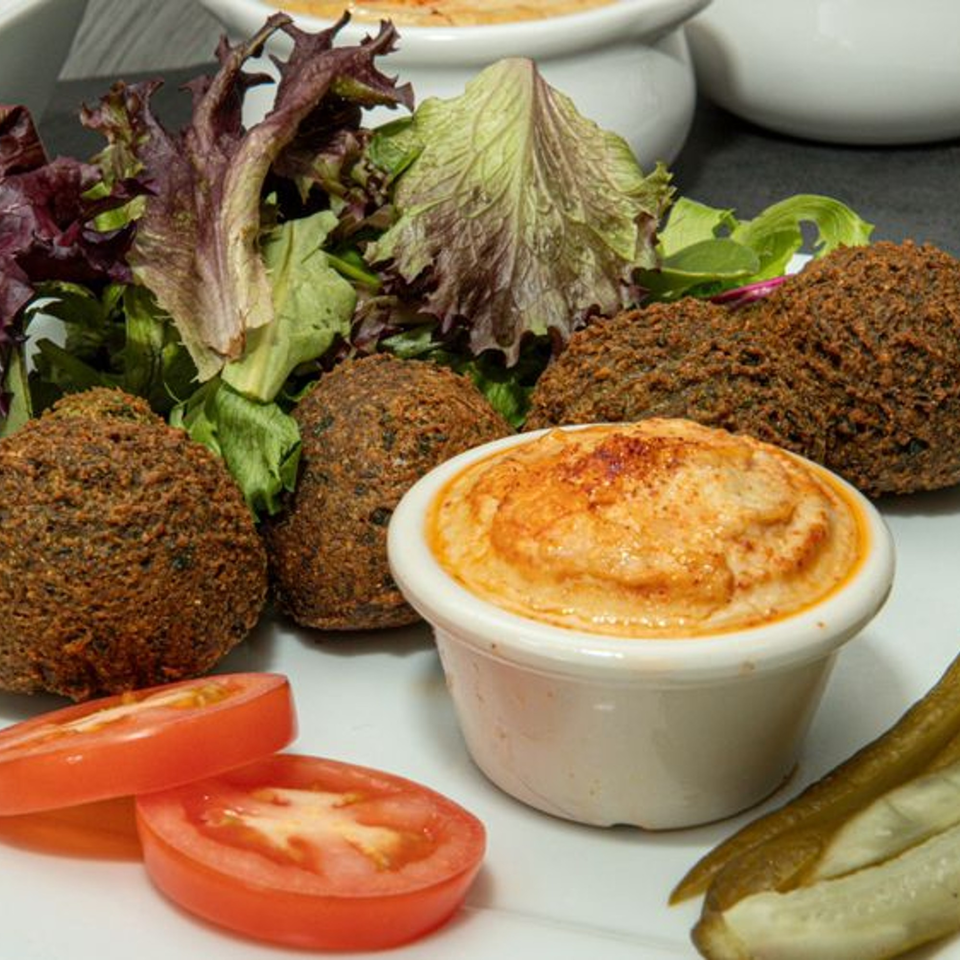Mediterranean falafel plate with hummus, fresh lettuce, tomato slices, and pickles from Kookoo Cafe.